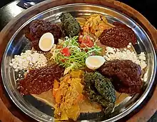 Doro WotA stew dish served with beef, lamb, chicken, eggs and variety of vegetables, on top of Injera flatbread.