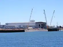 A long, wide building on the shore of a river, with the letters "ASC" on the visible faces.