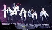 Seven persons performing on a stage dressed in black and white