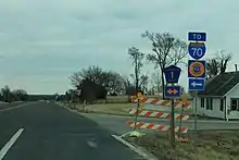 An intersection of a two-lane highway and another two-lane road in a rural area. Highway shields indicate both directions are County Route 1. A sign advises travelers to turn left (north) to reach Interstate 70, the Kansas Turnpike.