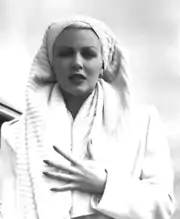 Woman in white wearing a towel on her head, clutching her chest