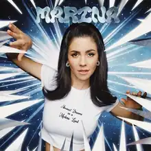 Marina, against a blue background and a pointy white border, wearing a white crop top displaying the song title.