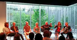 Mekons circa 2015, left to right: Lu Edmonds, Tom Greenhalgh, Steve Goulding, Sally Timms, Jon Langford, Susie Honeyman, Rico Bell (not pictured: Sarah Corina)