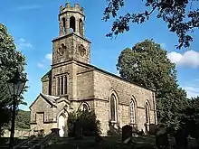 A single storey small church, constructed of sandstone, surrounded by trees