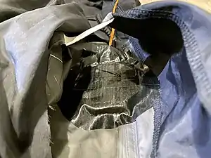 The inner taffeta lining cut open, exposing the outermost fabric from the inside which is then scored with a blade. The squib device is then aligned to the hole and attached with duct tape.