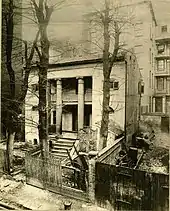 Black and white photograph of a small Greek revival house in an alleyway
