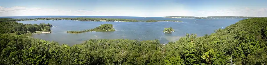 View in August from the now-closed tower.  Sawyer Harbor is in the foreground, with the western part of Sturgeon Bay in the background. The small island at right is Heaven On Earth Island, formerly Bug Island. The larger island to the left is Idyll Wood Island. Cabot Point is behind the two islands. It is part of the Idlewild area. In the far distance at center-right is the rock cut of the Old Stone Quarry on the northwest shore of Sturgeon Bay, once the largest in the state.