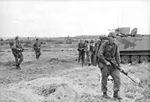A black and white image of New Zealand soldiers and an armoured personnel carrier during Operation Coburg